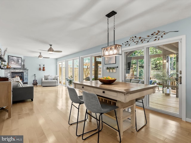 dining space with a stone fireplace, light wood-style floors, a ceiling fan, and baseboards