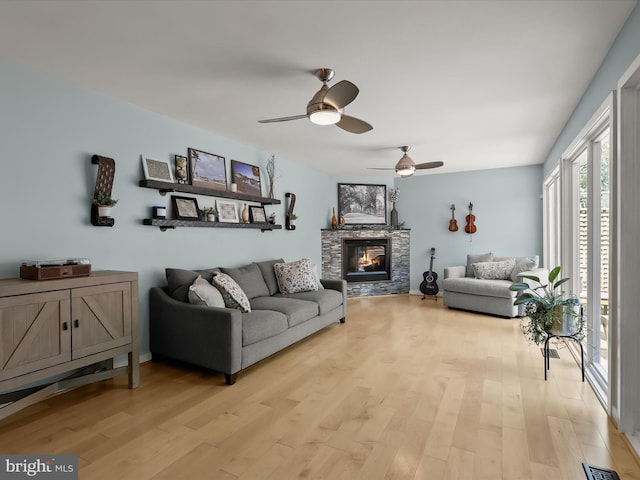 living room with light wood-style flooring, ceiling fan, and a stone fireplace