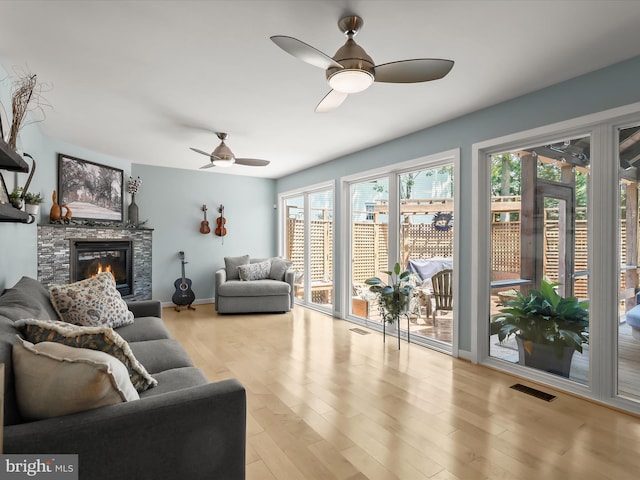 living room with a ceiling fan, wood finished floors, and a stone fireplace