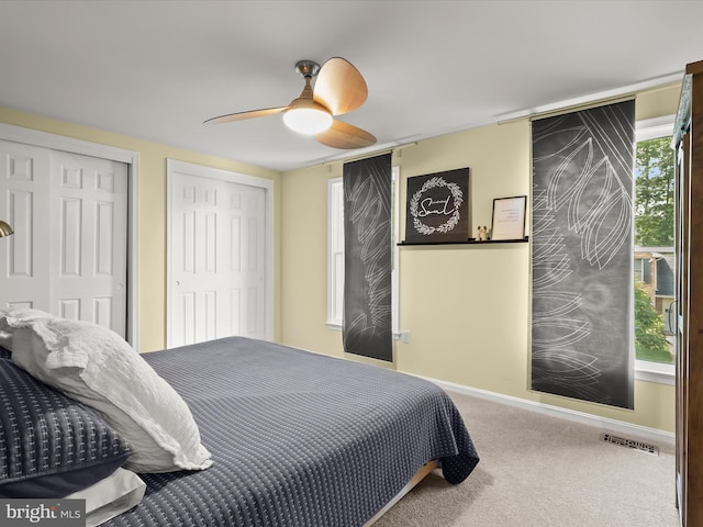 carpeted bedroom with two closets, baseboards, and a ceiling fan