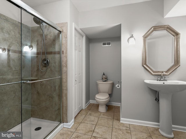 bathroom featuring a stall shower, toilet, tile patterned floors, baseboards, and a sink