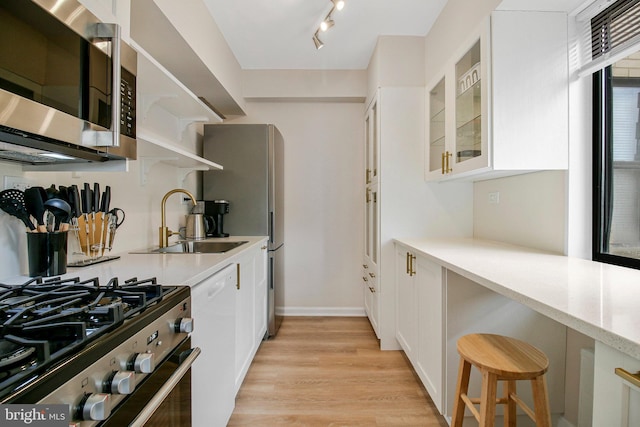 kitchen with white cabinets, stainless steel appliances, a sink, and light wood finished floors
