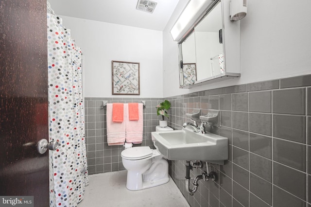 full bath with visible vents, a sink, toilet, tile walls, and wainscoting