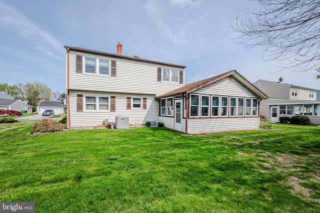 back of house with a sunroom, a chimney, and a yard