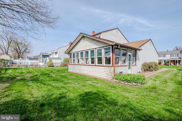 back of property with fence, a sunroom, a chimney, and a lawn