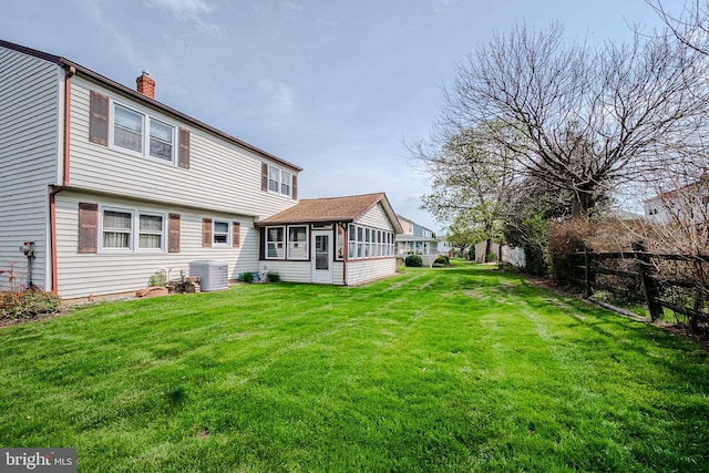 back of house featuring a sunroom, a lawn, fence, a chimney, and central AC unit