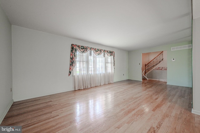unfurnished living room featuring wood finished floors, visible vents, and stairway