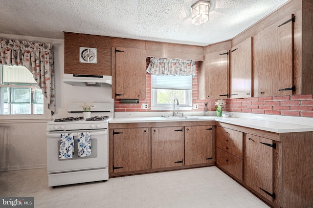 kitchen with under cabinet range hood, light countertops, white range with gas stovetop, and light floors