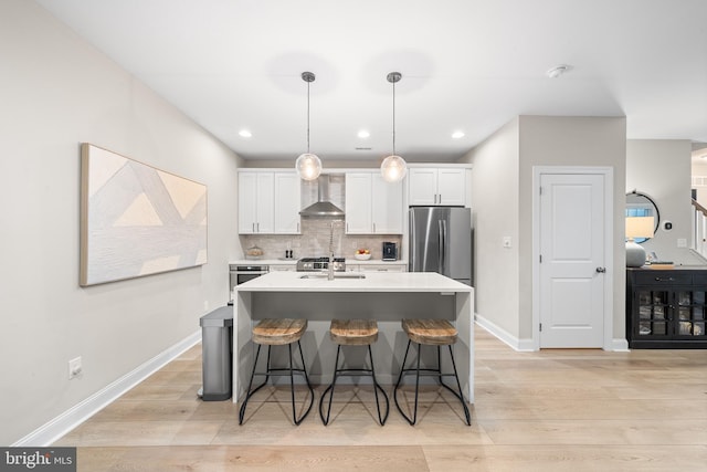 kitchen with white cabinets, wall chimney exhaust hood, a sink, freestanding refrigerator, and a kitchen breakfast bar
