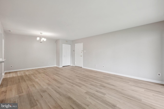 empty room featuring light wood-style flooring, a notable chandelier, and baseboards