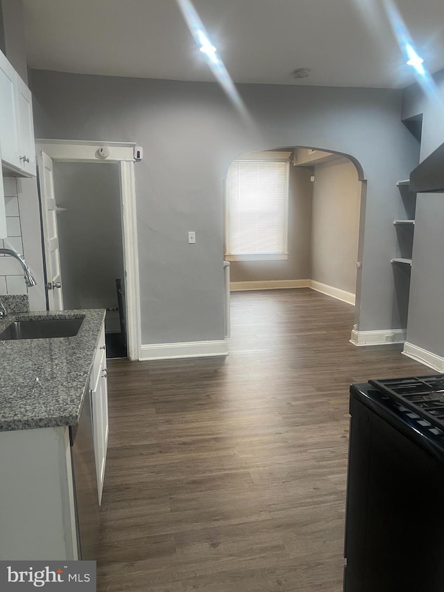 kitchen with stone countertops, baseboards, white cabinets, arched walkways, and a sink