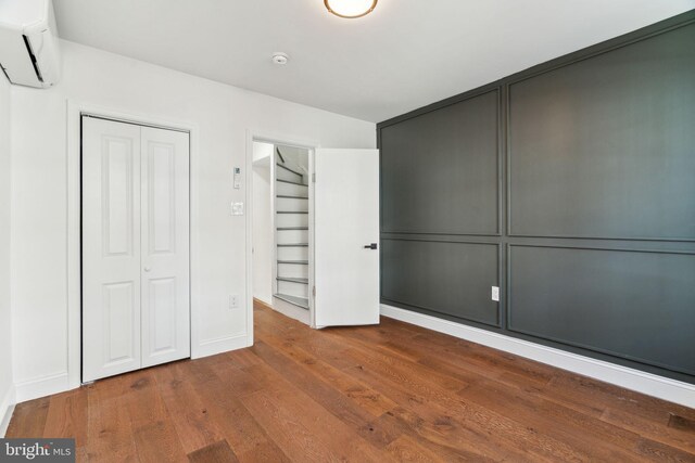 unfurnished bedroom featuring baseboards, a closet, a wall unit AC, and wood finished floors
