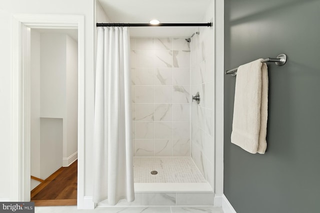 bathroom with baseboards, tiled shower, and marble finish floor