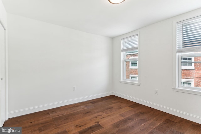 empty room featuring a wealth of natural light, baseboards, and dark wood-style floors
