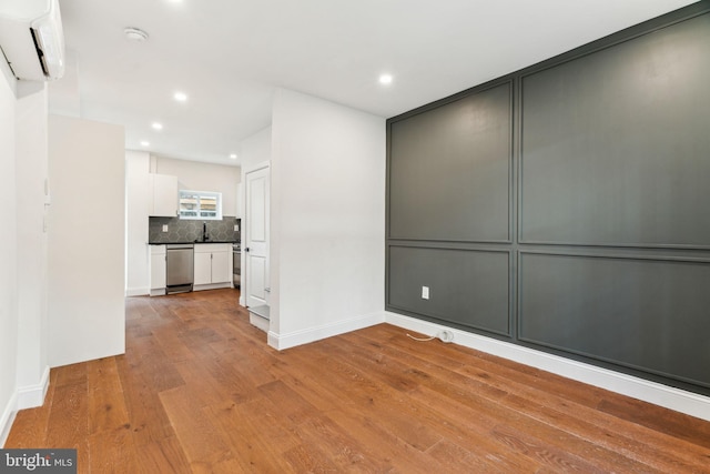 unfurnished room with light wood-style flooring, a wall unit AC, baseboards, and recessed lighting