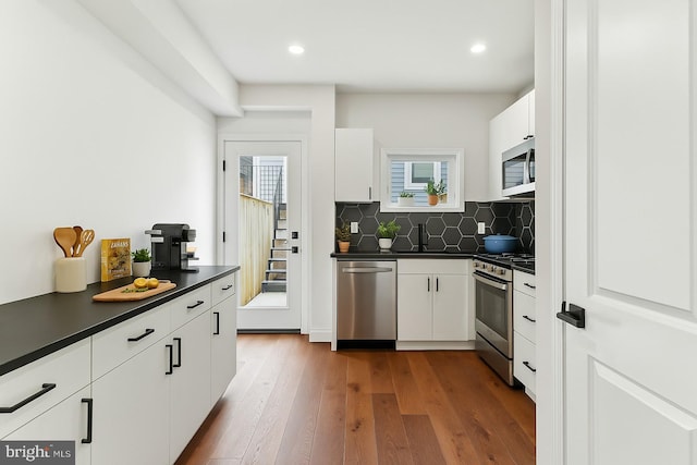 kitchen featuring stainless steel appliances, white cabinets, backsplash, and dark countertops