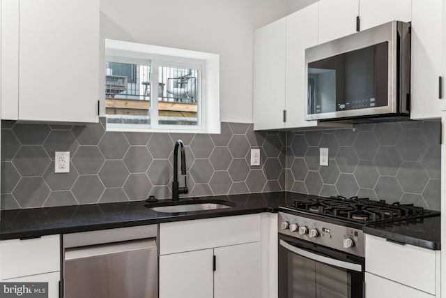 kitchen with backsplash, appliances with stainless steel finishes, a sink, and white cabinetry