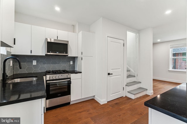 kitchen featuring a sink, appliances with stainless steel finishes, dark countertops, dark wood finished floors, and white cabinetry