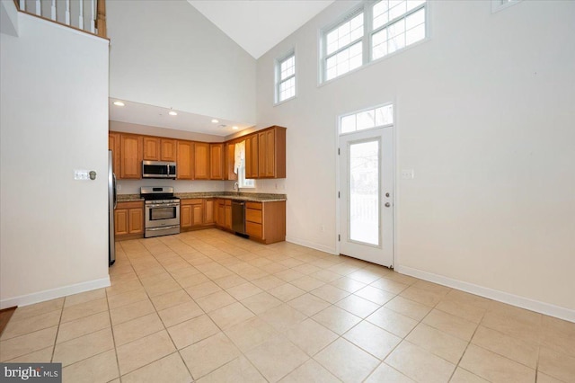 kitchen with baseboards, brown cabinets, appliances with stainless steel finishes, high vaulted ceiling, and a sink