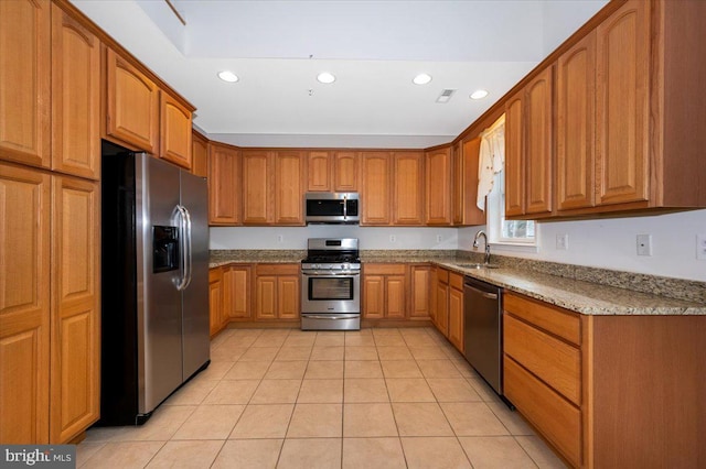 kitchen with light tile patterned floors, light stone countertops, brown cabinets, appliances with stainless steel finishes, and a sink