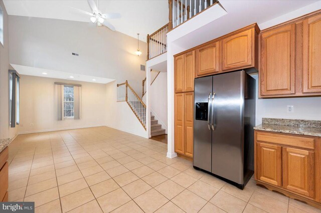 kitchen with stainless steel fridge with ice dispenser, light tile patterned floors, a ceiling fan, a high ceiling, and light stone counters
