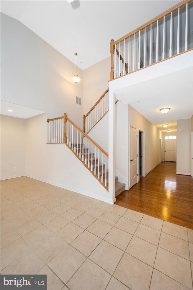 stairs featuring baseboards, tile patterned floors, a towering ceiling, and visible vents