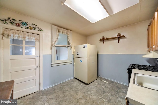 kitchen featuring light countertops, freestanding refrigerator, a sink, and range with gas stovetop