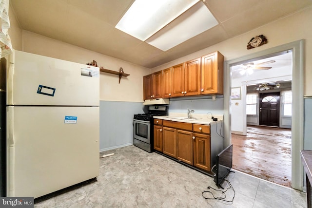 kitchen with a sink, light countertops, ceiling fan, freestanding refrigerator, and gas stove