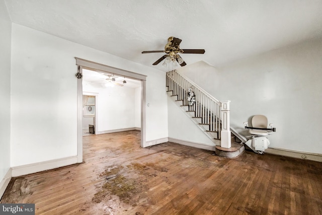 unfurnished living room featuring ceiling fan, wood-type flooring, baseboards, and stairs