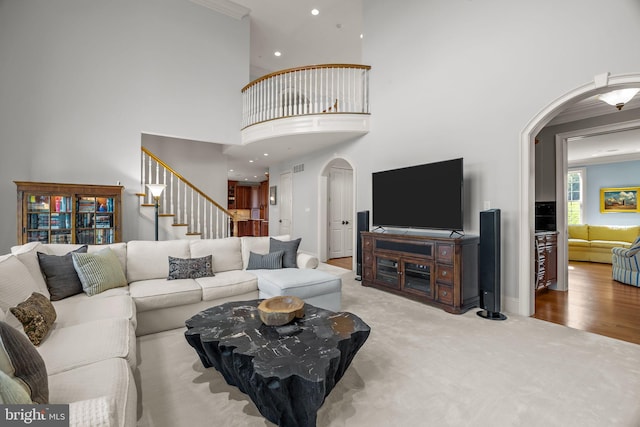 carpeted living room featuring stairway, arched walkways, a high ceiling, and crown molding