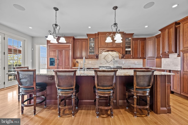kitchen featuring tasteful backsplash, a kitchen island with sink, paneled fridge, a sink, and light wood-type flooring
