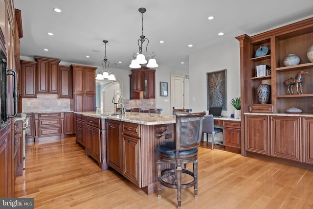 kitchen with tasteful backsplash, recessed lighting, an island with sink, light wood finished floors, and a sink