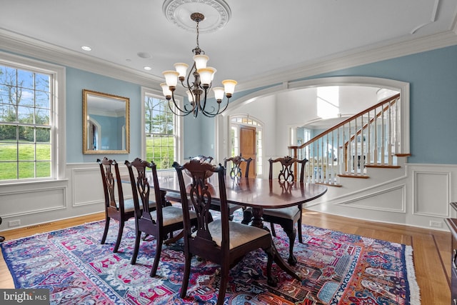 dining room with a notable chandelier, a wainscoted wall, ornamental molding, arched walkways, and wood finished floors