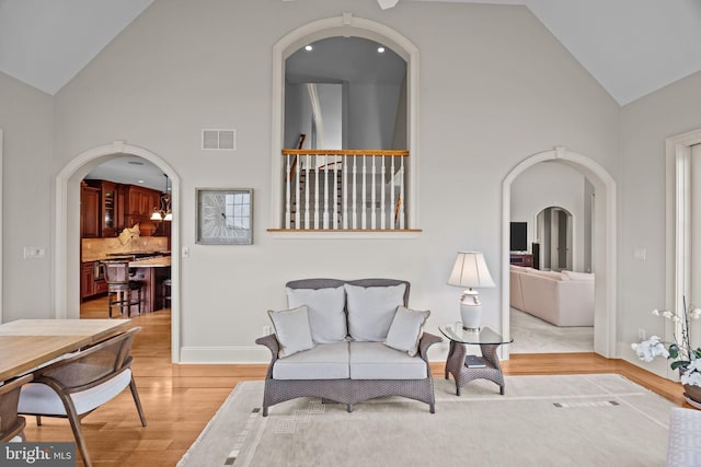 sitting room with visible vents, baseboards, high vaulted ceiling, and light wood-type flooring