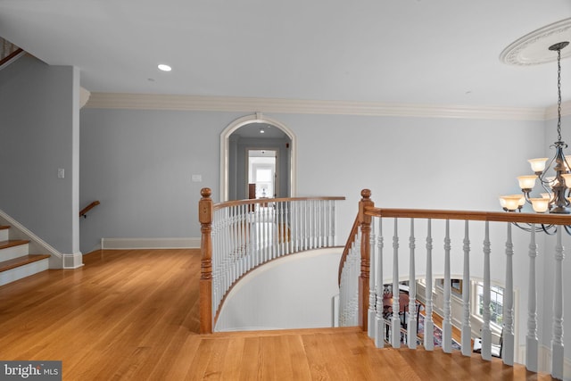 stairs with an inviting chandelier, wood finished floors, ornamental molding, and baseboards