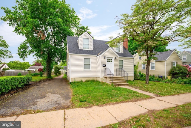 cape cod-style house featuring a front lawn, a chimney, roof with shingles, and fence