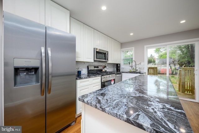 kitchen with light wood-type flooring, stainless steel appliances, white cabinets, and dark stone counters