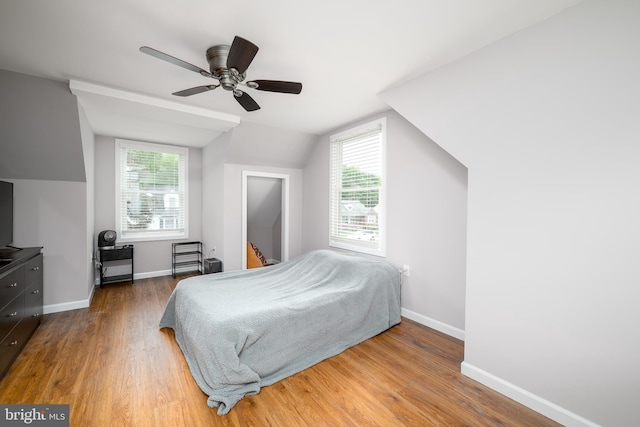 bedroom with multiple windows, wood finished floors, vaulted ceiling, and baseboards
