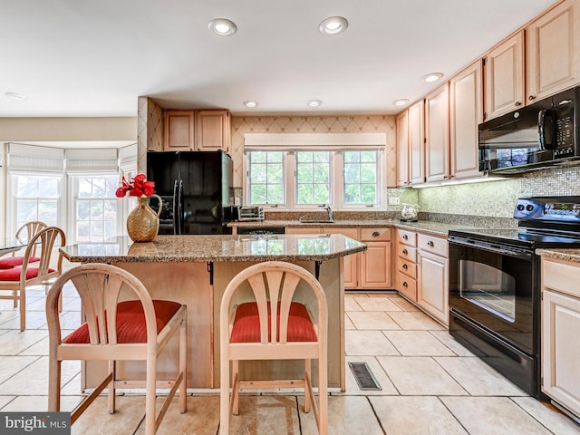 kitchen with light brown cabinetry, a kitchen breakfast bar, backsplash, a kitchen island, and black appliances
