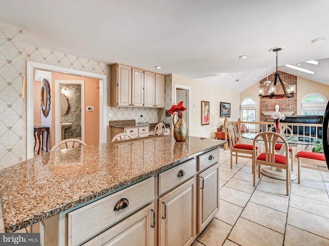 kitchen featuring an inviting chandelier, lofted ceiling, light brown cabinets, light stone countertops, and a center island