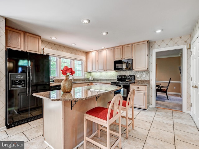 kitchen featuring a kitchen island, light stone counters, light tile patterned floors, and black appliances
