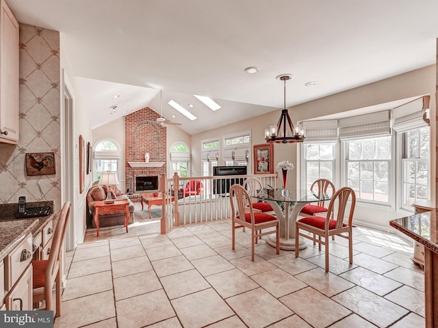 dining room featuring a chandelier, plenty of natural light, vaulted ceiling with skylight, and a fireplace