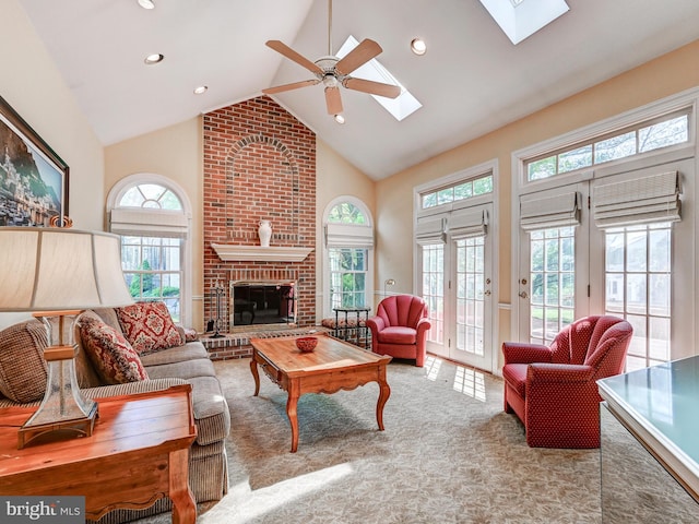 living area featuring a ceiling fan, a skylight, a brick fireplace, high vaulted ceiling, and carpet flooring