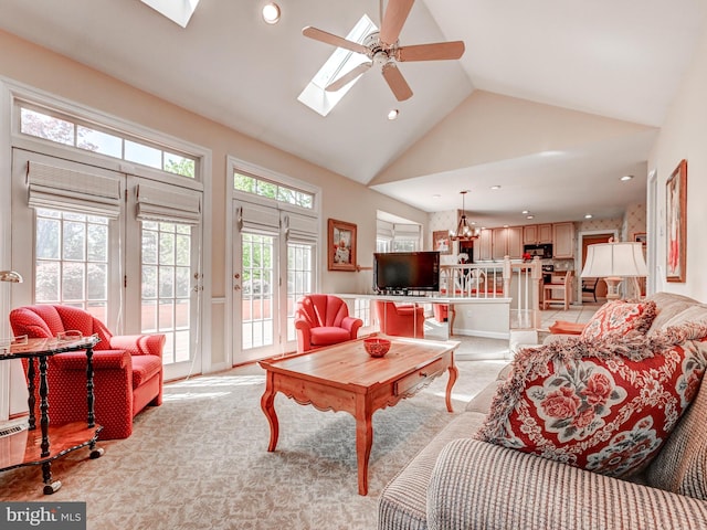 living area featuring light colored carpet, ceiling fan, a skylight, and high vaulted ceiling