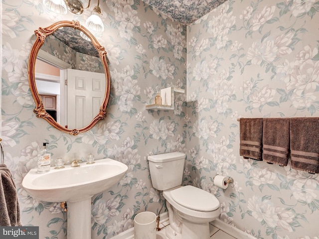 bathroom featuring toilet, wallpapered walls, and baseboards