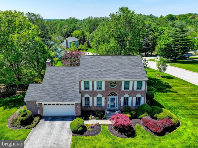 colonial house featuring a front lawn, brick siding, a garage, a chimney, and driveway