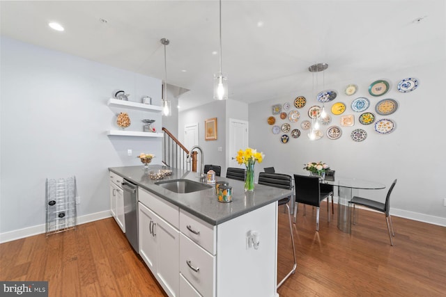 kitchen featuring a peninsula, wood finished floors, stainless steel dishwasher, and a sink
