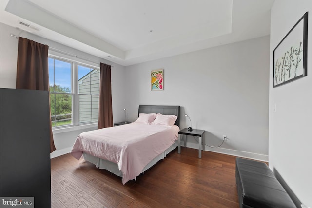 bedroom featuring baseboards, wood finished floors, visible vents, and a raised ceiling