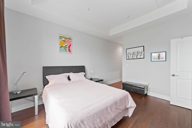 bedroom featuring baseboards, wood finished floors, and a raised ceiling