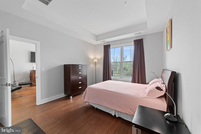 bedroom featuring visible vents, baseboards, wood finished floors, and a raised ceiling
